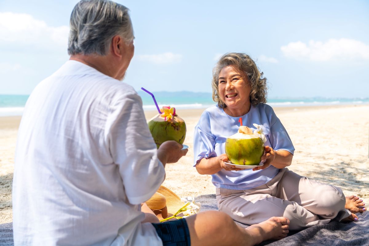 Elderly couple enjoying fresh coconuts on a tropical Phuket beach